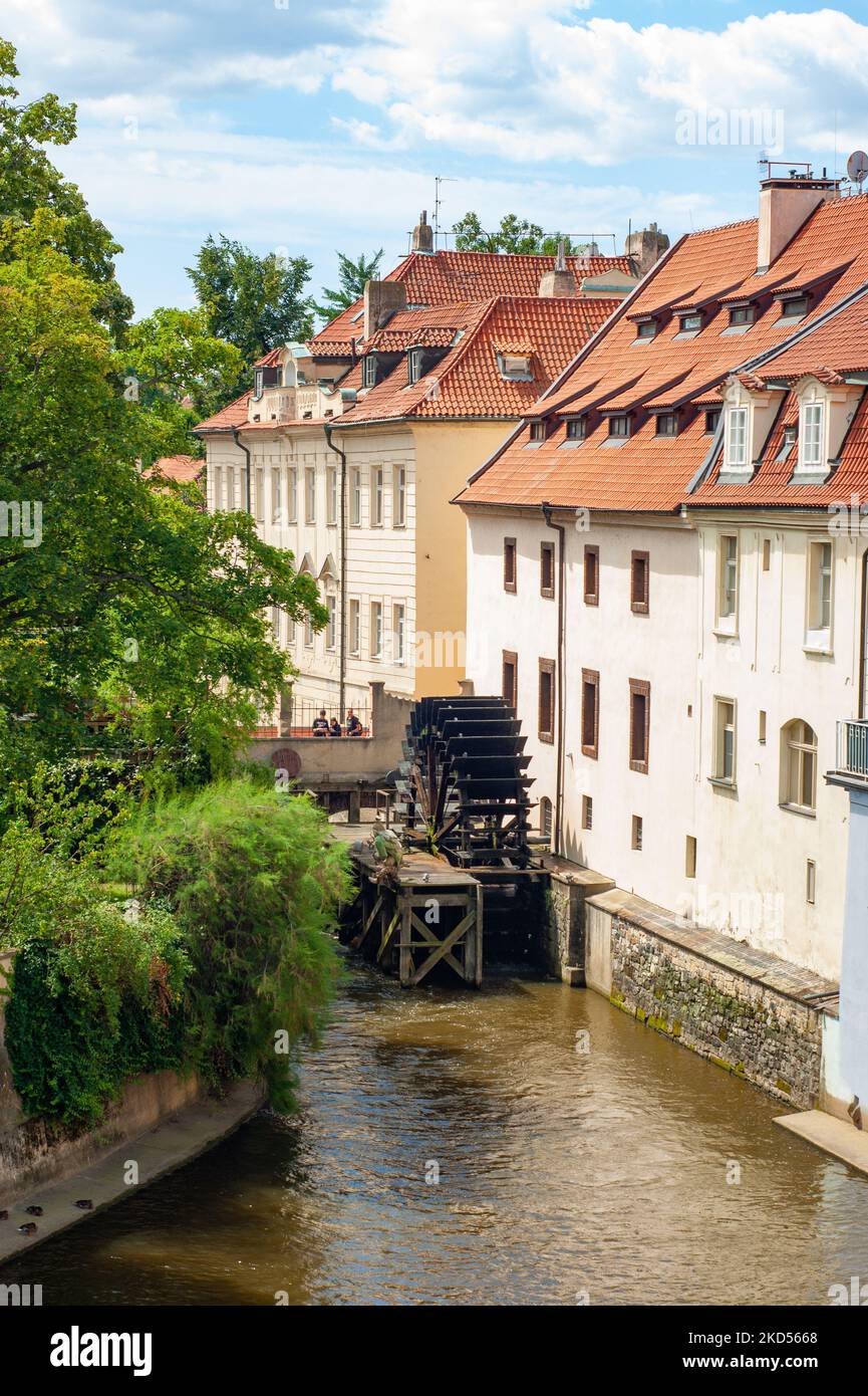 Gebäude mit roten Ziegeldächern. Die Ansicht ist von der Karlsbrücke, Prag, Tschechische Republik, aufgenommen. Sie sehen Fluss oder Kanal mit altem Wasserrad oder Paddelrad. Stockfoto