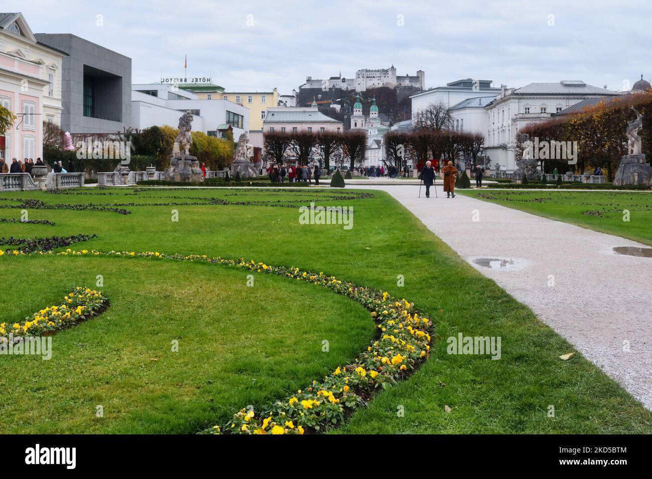 Salzburg, Österreich - 30. November 2019: Garten mit grünem Gras, Blumen, Statuen und Spazierwegen in Salzburg, Österreich mit einer Kaste auf einem Hügel in der Stockfoto