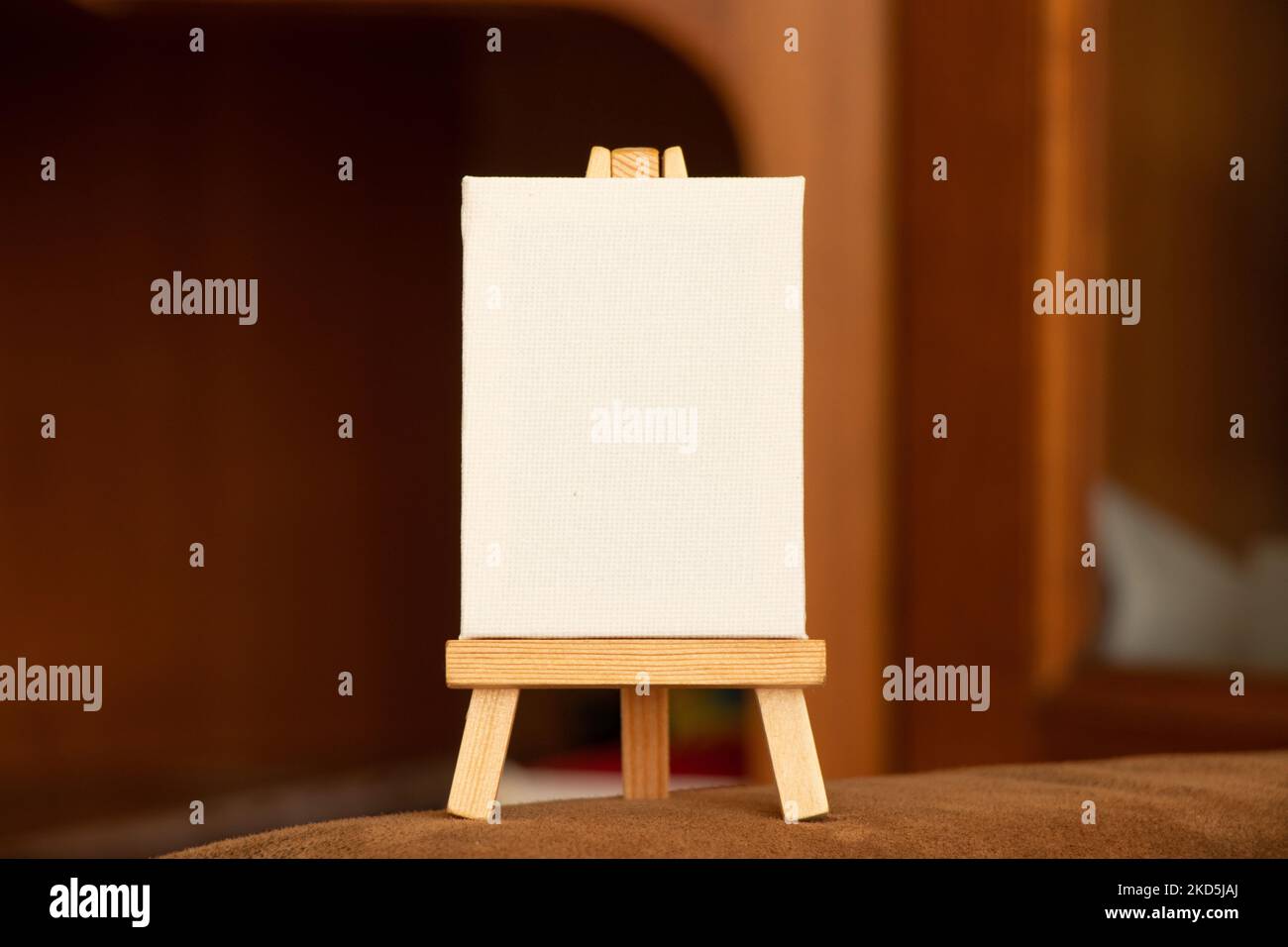 Eine leere weiße Palette steht auf einer hölzernen Staffelei auf einem Tisch auf braunem Hintergrund, eine Palette und Platz für Text Stockfoto