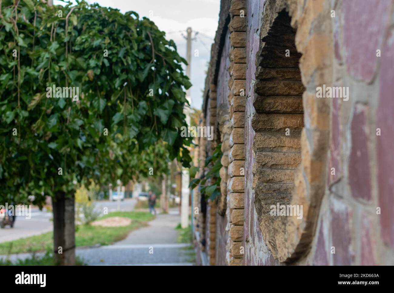 Authentischer Steinzaun vor dem Hintergrund einer ruhigen grünen Straße einer kleinen Stadt Stockfoto