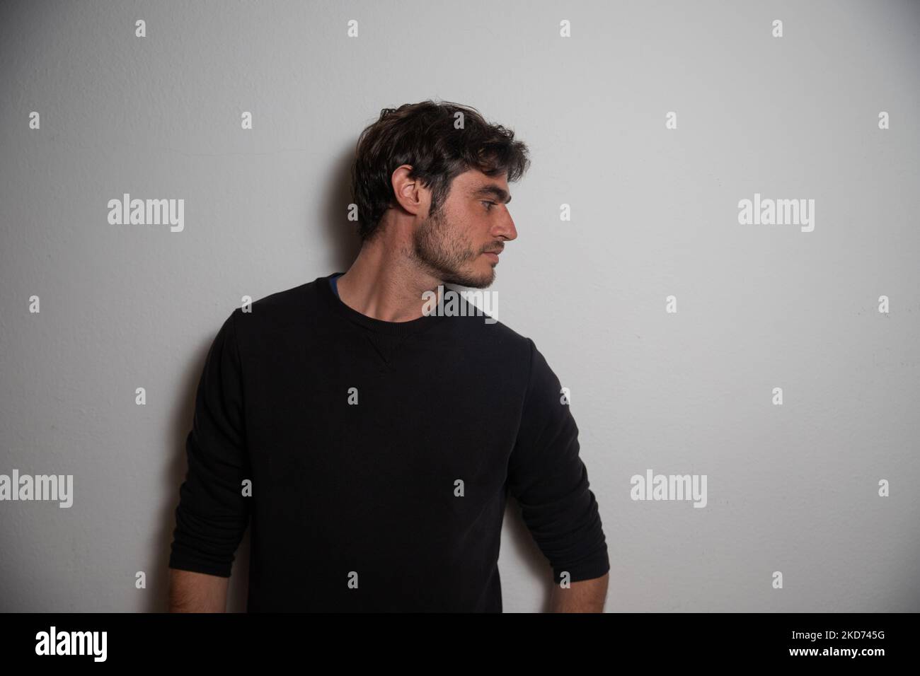 Porträt eines jungen kaukasischen Mannes in seiner 30s lehnt an der Wand im Studio. Stockfoto