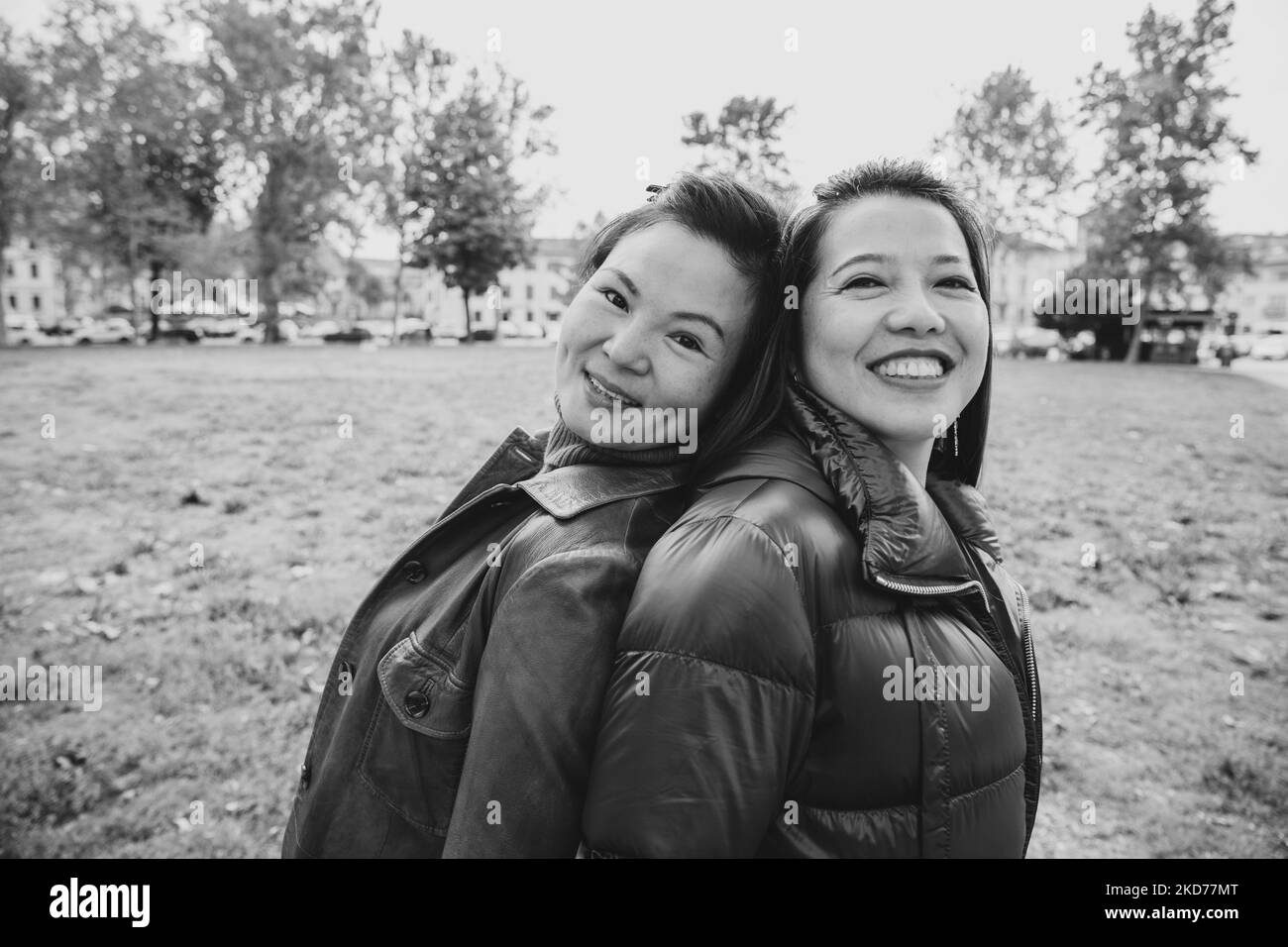 Schwarz-weiß-Aufnahme von zwei lächelnden chinesischen Frauen, die sich auf ihren Rücken lehnen. Stockfoto