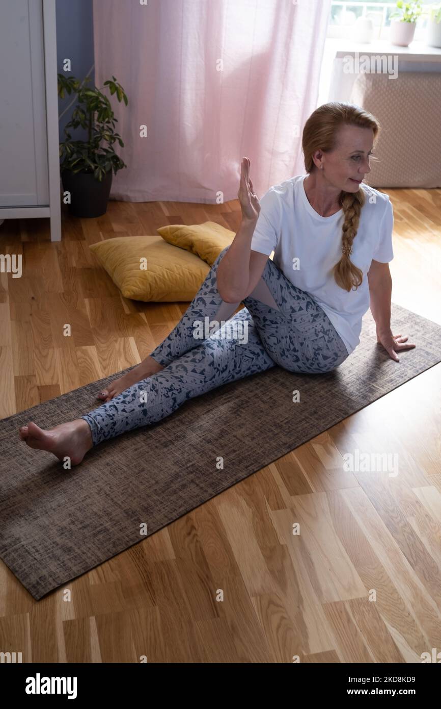 Reife, weiße Frau, die zu Hause eine gedrehte Yoga-Pose macht Stockfoto