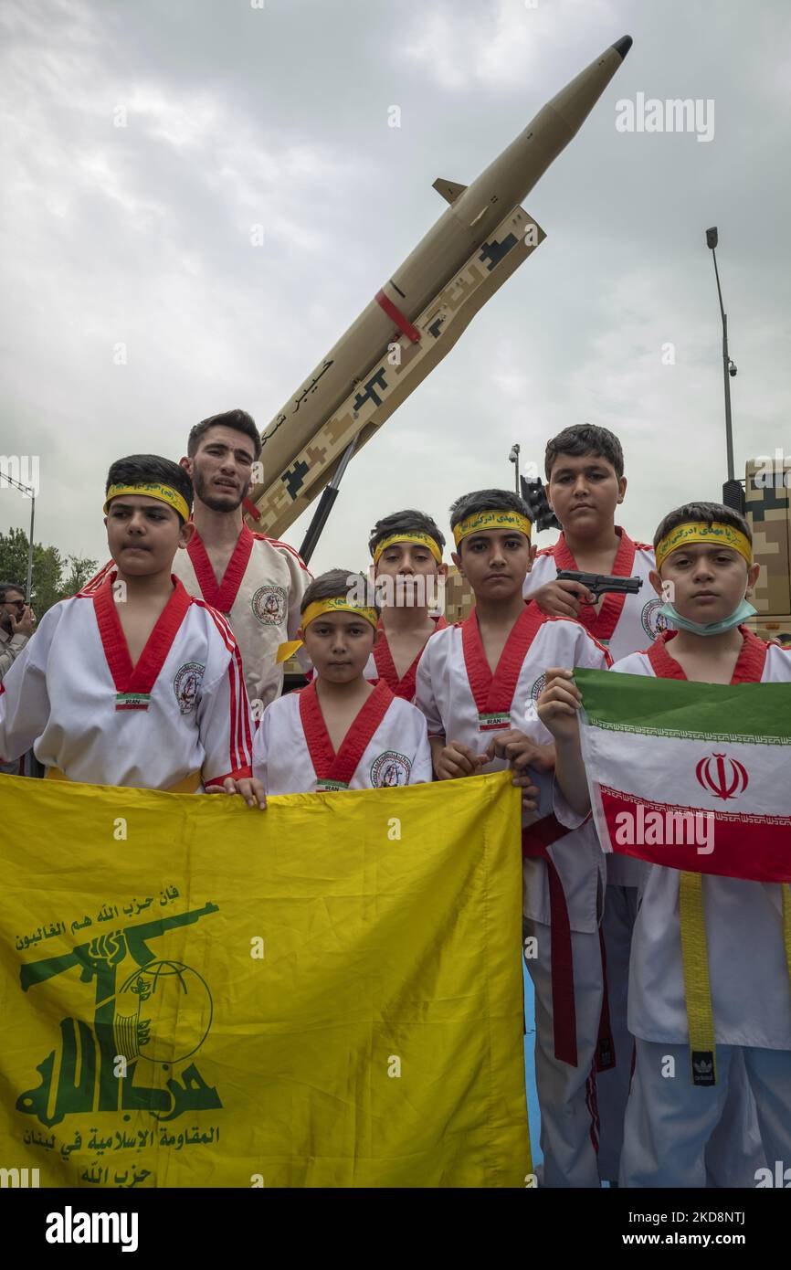 Eine Gruppe iranischer Sportler, die eine iranische Flagge und eine Flagge der libanesischen Hisbollah halten, während sie während einer Kundgebung zum Gedenken an den Internationalen Quds-Tag, der auch als Jerusalem-Tag bekannt ist, am 29. April 2022 auf einer iranischen Kheibar-Shekan-ballistischen Rakete in der Innenstadt von Teheran stehen. (Foto von Morteza Nikoubazl/NurPhoto) Stockfoto