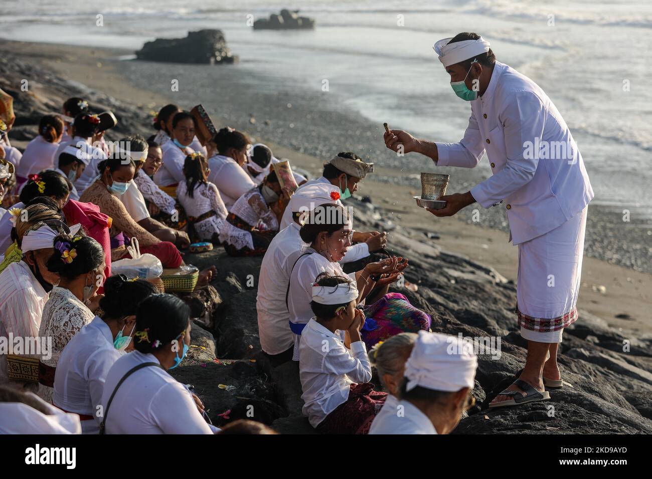 Balinesische Hindu-Anhänger erhalten heiliges Wasser, während sie während der Melasti beten, einer Reinigungszeremonie vor Nyepi an einem Strand in Bali, Indonesien, am 1. März 2022. Balinesische Hindus trugen in überwiegend weißer Kleidung heilige Bildnisse von Göttern und Göttinnen und rituelle Utensilien von ihren Dorftempeln zum Strand, um eine Reinigungszeremonie, das sogenannte Melasti-Ritual, durchzuführen. Balinesische Hindus glauben, dass das Melasti-Ritual vor dem Nyepi-Tag, dem Tag der Stille, ein muss ist, um die Seele und die Natur zu reinigen, die übernatürliche Kraft der heiligen Tempelobjekte aufzuladen und die te zu reinigen Stockfoto