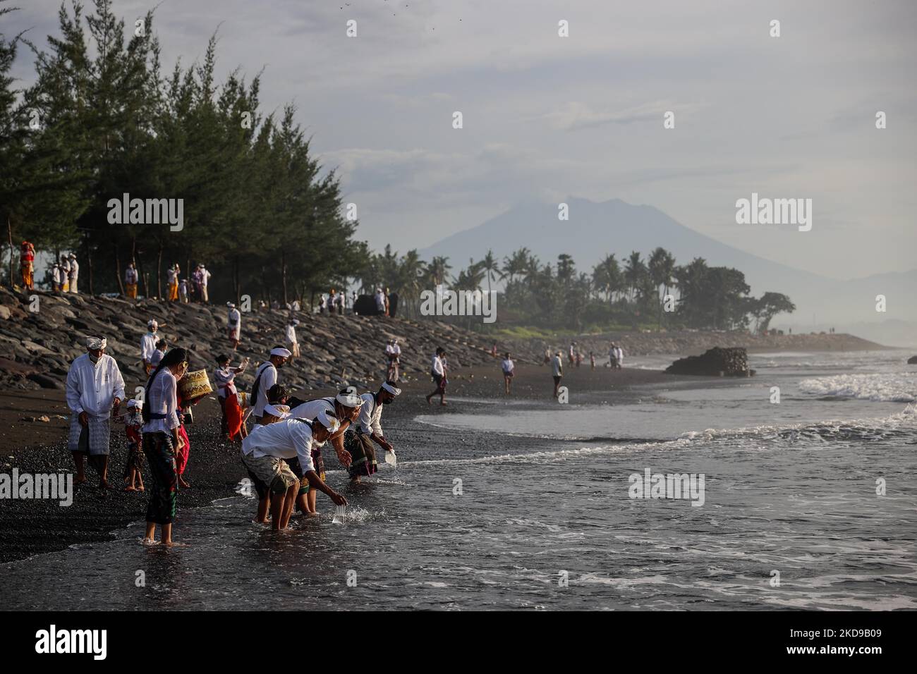 Balinesische Hindu-Anhänger waschen ihr Gesicht mit Meerwasser, während sie während der Melasti beten, einer Reinigungszeremonie vor Nyepi an einem Strand in Bali, Indonesien, am 1. März 2022. Balinesische Hindus trugen in überwiegend weißer Kleidung heilige Bildnisse von Göttern und Göttinnen und rituelle Utensilien von ihren Dorftempeln zum Strand, um eine Reinigungszeremonie, das sogenannte Melasti-Ritual, durchzuführen. Balinesische Hindus glauben, dass das Melasti-Ritual vor dem Nyepi-Tag, dem Tag der Stille, ein muss ist, um die Seele und die Natur zu reinigen, die übernatürliche Kraft der heiligen Tempelobjekte aufzuladen und c Stockfoto