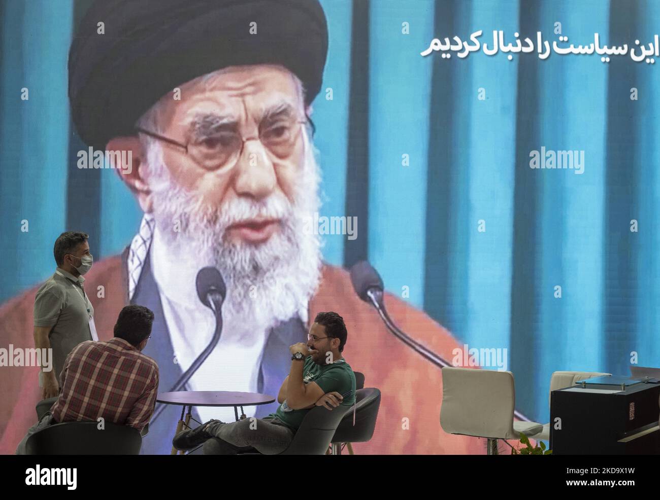 Zwei Jahre nach dem Ausbruch der COVID-19 im Iran sprechen Mitglieder des iranischen Forschungsinstituts für die Erdölindustrie miteinander, während auf der Internationalen Ausstellung für Öl, Gas, Raffination und Petrochemie 26. in Teheran am 13. Mai ein riesiges Porträt des iranischen Obersten Führers Ayatollah Ali Khamenei gezeigt wird. 2022. (Foto von Morteza Nikoubazl/NurPhoto) Stockfoto