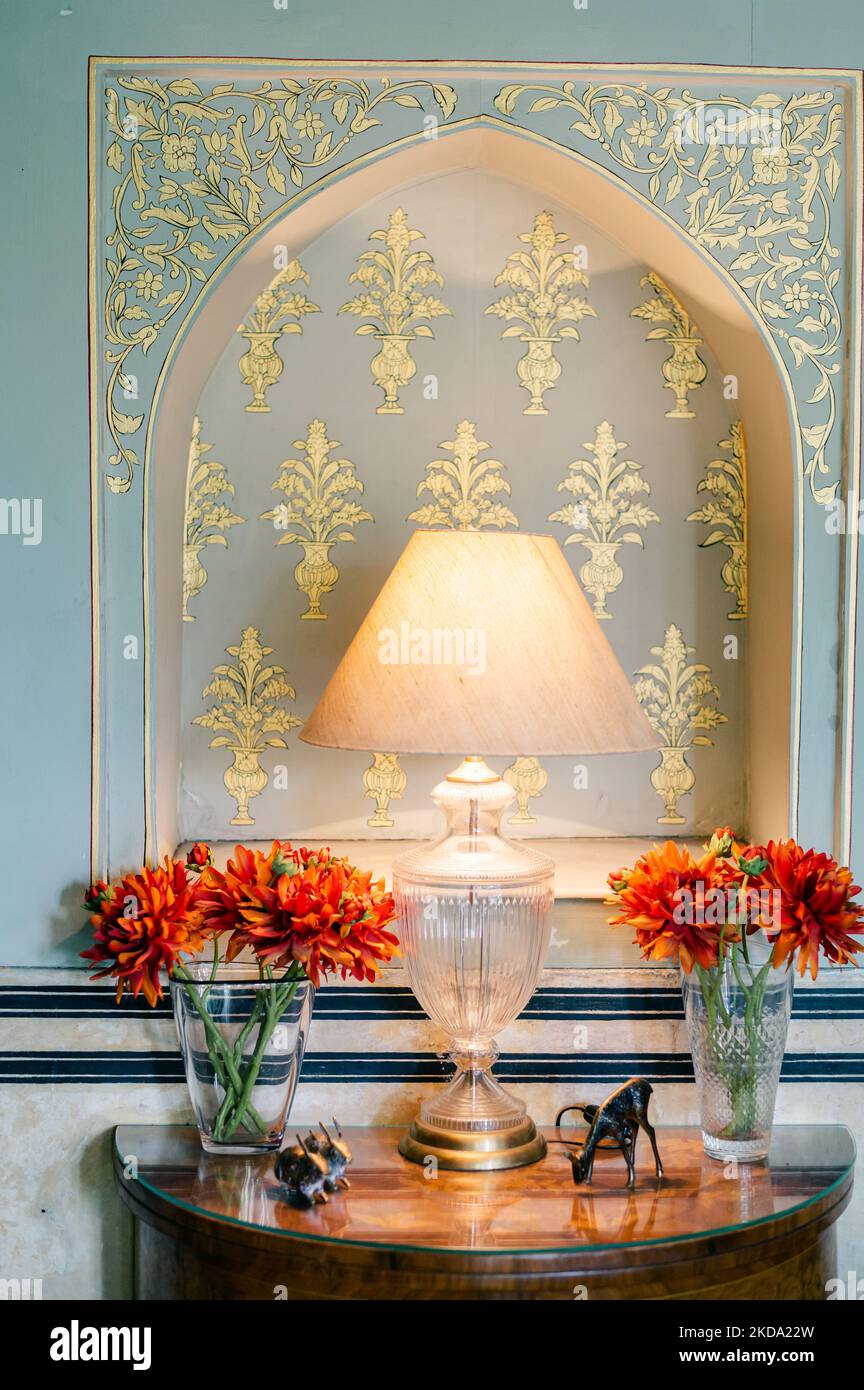 Eine vertikale Aufnahme einer auf dem Tisch getunten Lampe mit Blumen an der Wand mit Vintage-Motiven Stockfoto