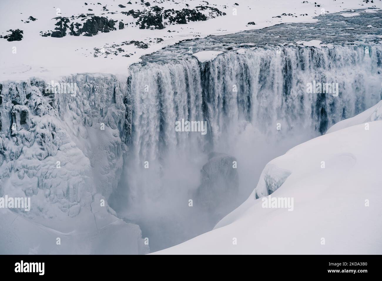 Eine Luftaufnahme des fließenden Wasserfalls von Felsen umgeben von schneebedeckten Feld Stockfoto