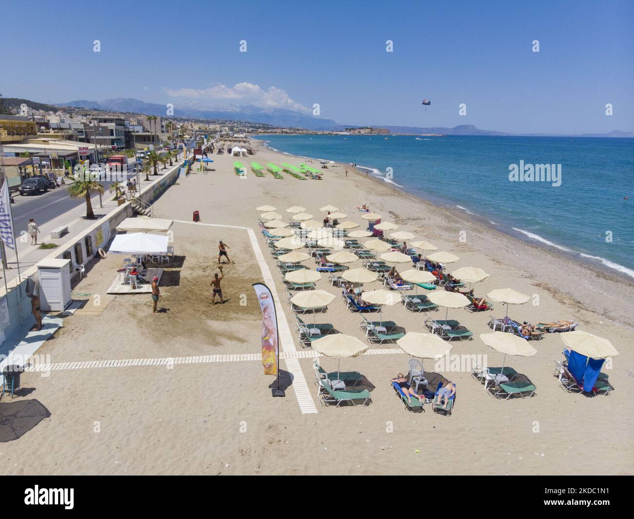 Luftaufnahmen von einer Drohne der Küste der Stadt Rethymno mit dem langen Strand und den Strandbars auf der Insel Creta. Man sieht die Menschen an der Strandbar unter dem Sonnenschirm die Sonne genießen oder im kristallklaren Meer schwimmen. Rethymno ist eine historische mediterrane Strandstadt an der Nordküste Kretas, die an der Ägäis liegt und 40,000 Einwohner zählt. Ein touristisches Ziel mit einem historischen venezianischen Hafen und einer Stadt, archäologischen Stätten, endlosen Sandstränden, Wassersportmöglichkeiten, schönen, traditionellen Tavernen und einer großen Auswahl an Hotels. Der Tourismus kehrt zurück, und die Vorbehalte steigen Stockfoto