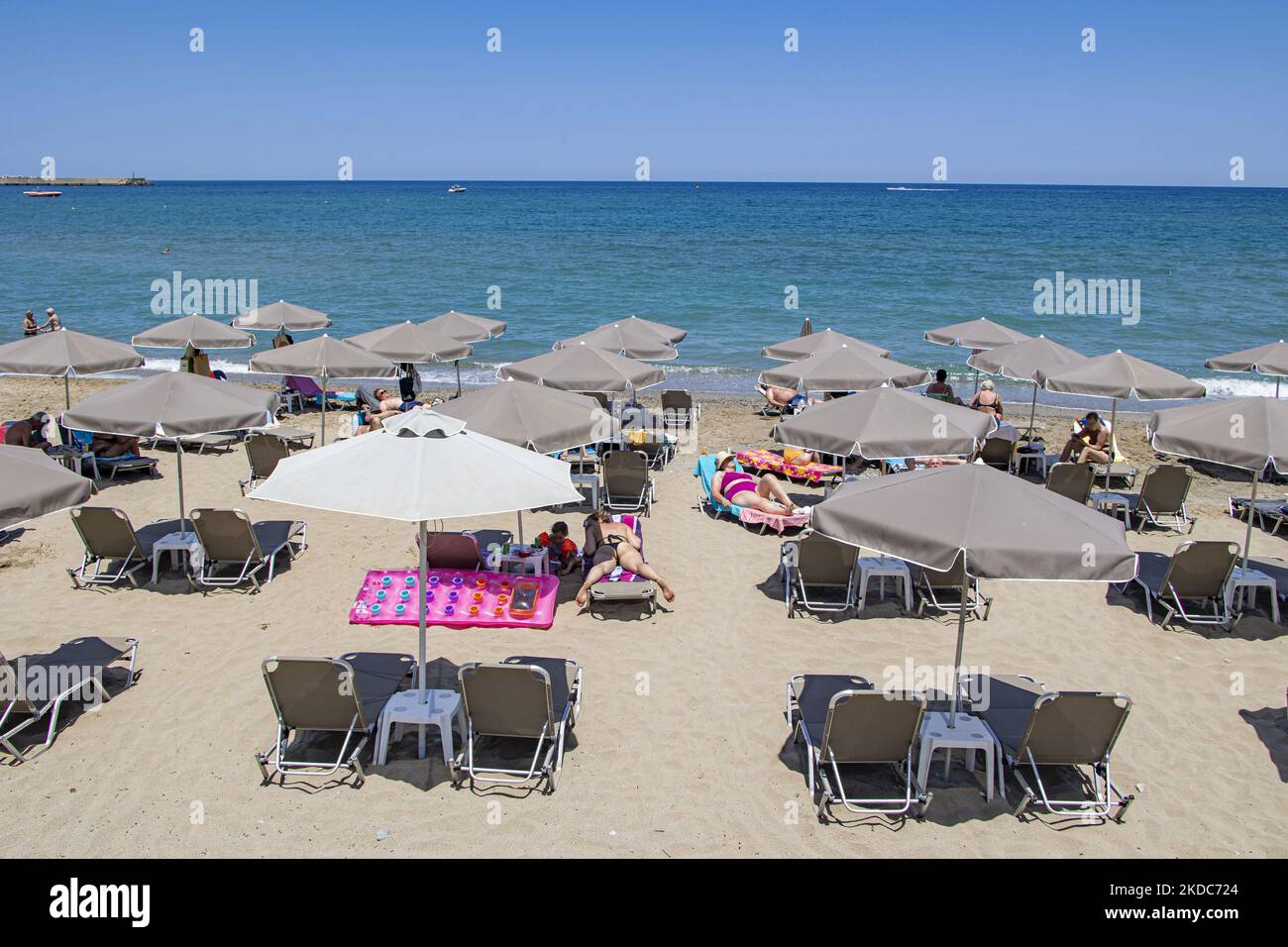 Tourismus in Griechenland. Die Küste der Stadt Rethymno mit dem langen Sandstrand und den Strandbars auf der Insel Creta mit den Bergen im Hintergrund. Man sieht die Menschen beim Sonnenbaden in Badeanzug, Badeanzug, Bikini, beim Sonnenbaden unter dem Sonnenschirm an der Strandbar auf einer Sonnenliege und beim Schwimmen im kristallklaren Meer. Rethymno ist eine historische mediterrane Strandstadt an der Nordküste Kretas, die an der Ägäis liegt und 40,000 Einwohner zählt. Ein touristisches Ziel mit einem historischen venezianischen Hafen und einer Stadt, archäologischen Stätten, endlosen Sandstränden, Wassersportmöglichkeiten, schönen schönen T Stockfoto