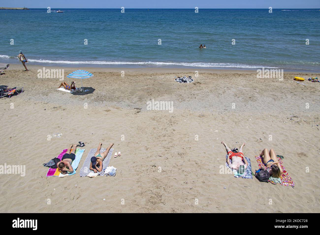 Tourismus in Griechenland. Die Küste der Stadt Rethymno mit dem langen Sandstrand und den Strandbars auf der Insel Creta mit den Bergen im Hintergrund. Man sieht die Menschen beim Sonnenbaden in Badeanzug, Badeanzug, Bikini, beim Sonnenbaden unter dem Sonnenschirm an der Strandbar auf einer Sonnenliege und beim Schwimmen im kristallklaren Meer. Rethymno ist eine historische mediterrane Strandstadt an der Nordküste Kretas, die an der Ägäis liegt und 40,000 Einwohner zählt. Ein touristisches Ziel mit einem historischen venezianischen Hafen und einer Stadt, archäologischen Stätten, endlosen Sandstränden, Wassersportmöglichkeiten, schönen schönen T Stockfoto