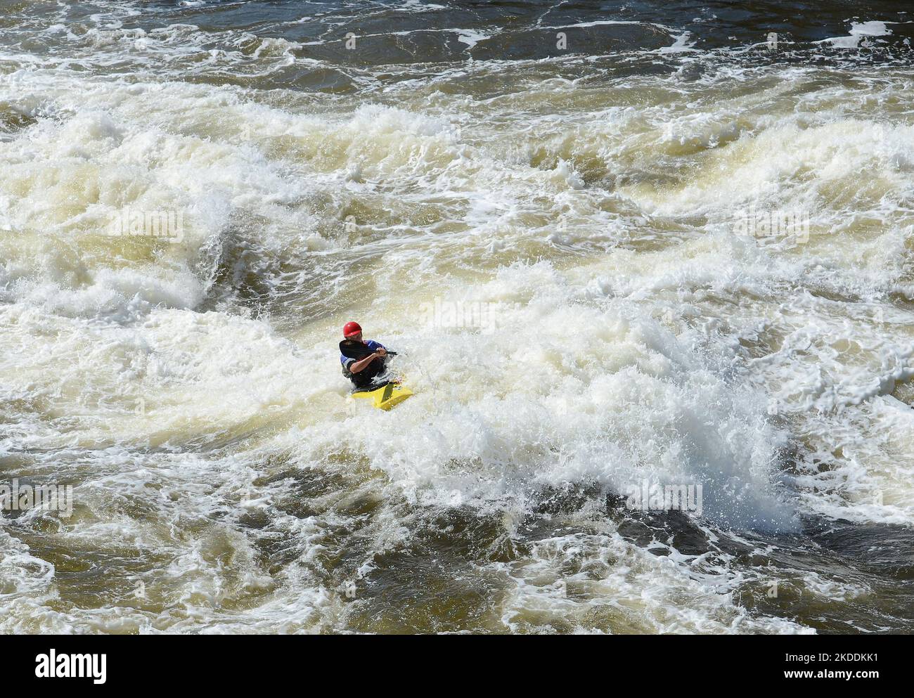 Kajakfahren in sehr rauen Stromschnellen. Der Fluss ist heftig mit vielen turbulenten Wellen und Spray. Das Gesicht der Person im Kajak ist nicht erkennbar. Stockfoto