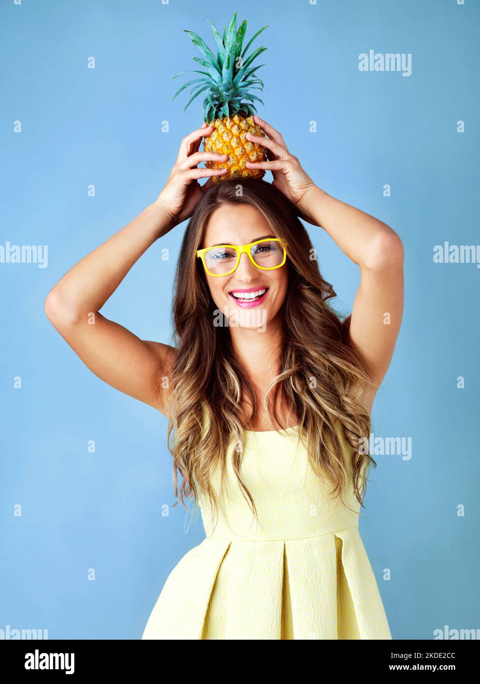 Hallo Sommer, ich bin bereit für dich. Studioaufnahme einer jungen Frau, die auf ihrem Kopf eine Ananas vor blauem Hintergrund balanciert. Stockfoto