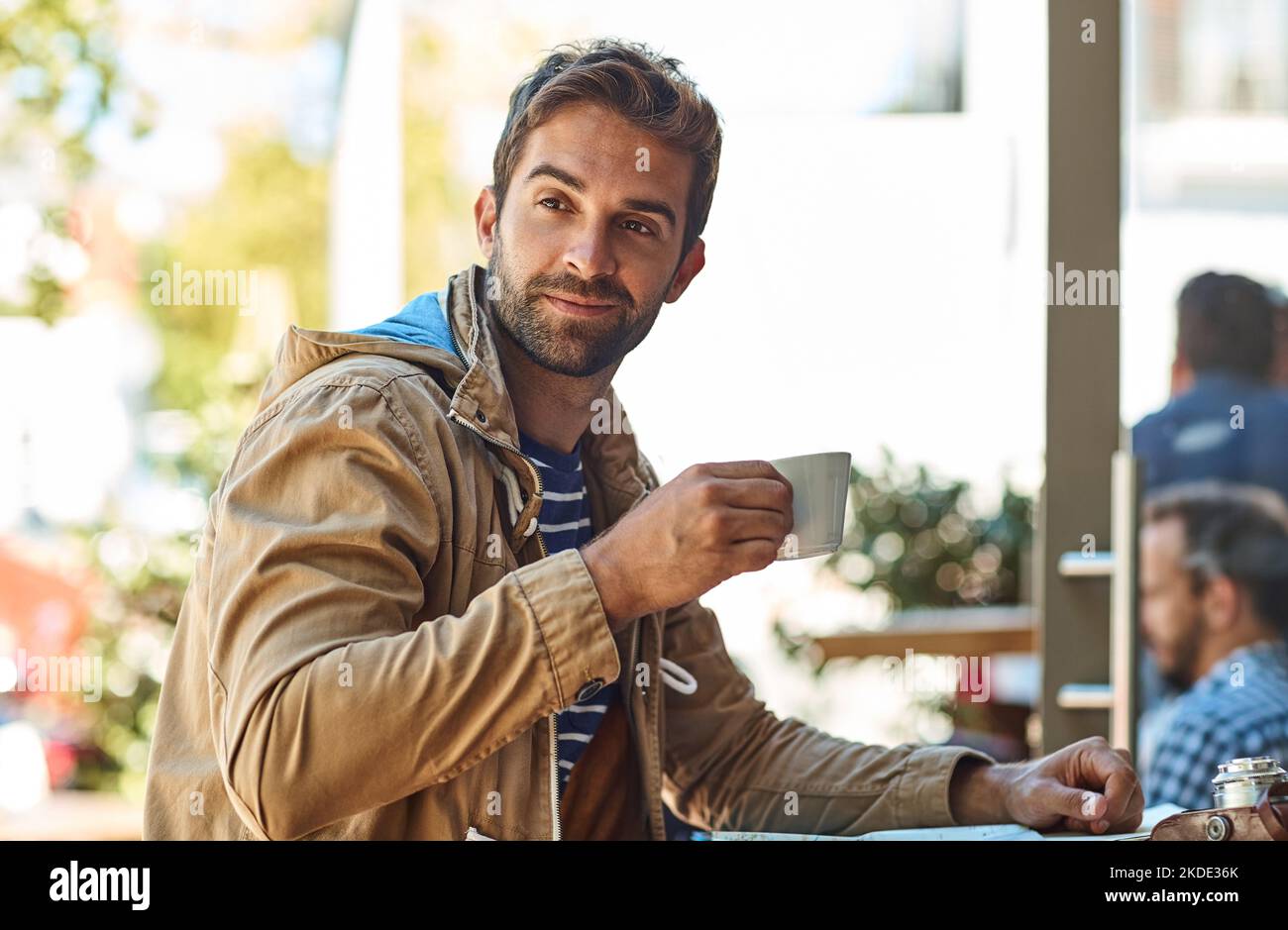 Nur eine kurze Aufladung, dann geht die Erkundung weiter. Ein entspannter Tourist, der eine Tasse Kaffee in einem Straßencafé genießt. Stockfoto