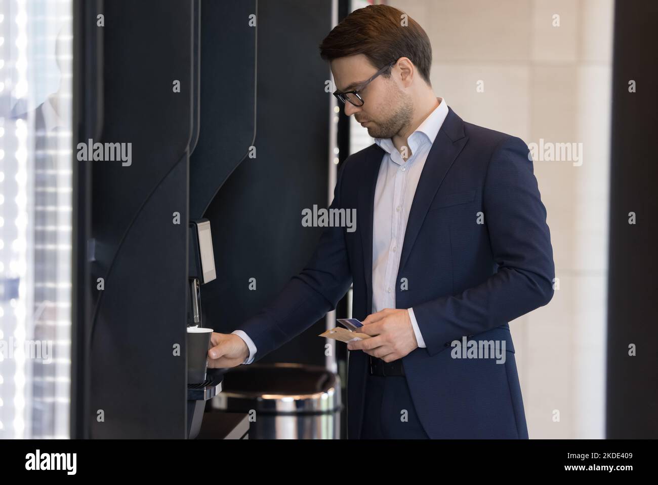 Der Geschäftsmann in Anzug gießt Kaffee und benutzt im Büro einen Verkaufsautomaten Stockfoto