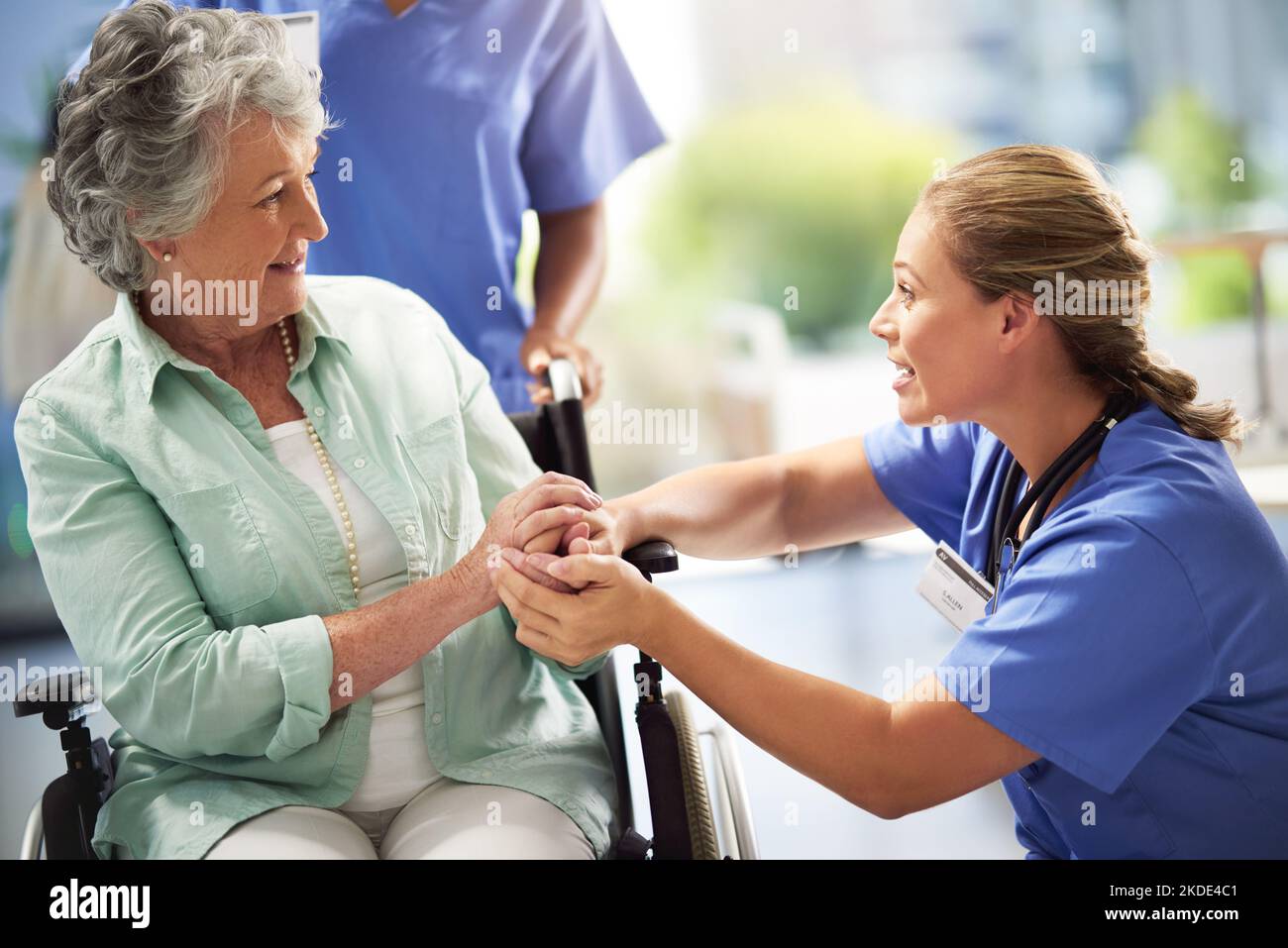 Bei uns sind Sie in guten Händen. Ein Arzt hält sich mit einer älteren Frau im Rollstuhl die Hände. Stockfoto