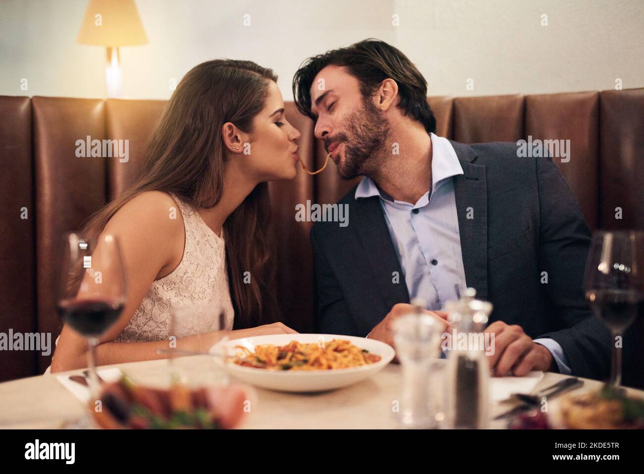 In der Mitte wird es köstlich. Ein junges Paar teilt sich Spaghetti während eines romantischen Abendessens in einem Restaurant. Stockfoto