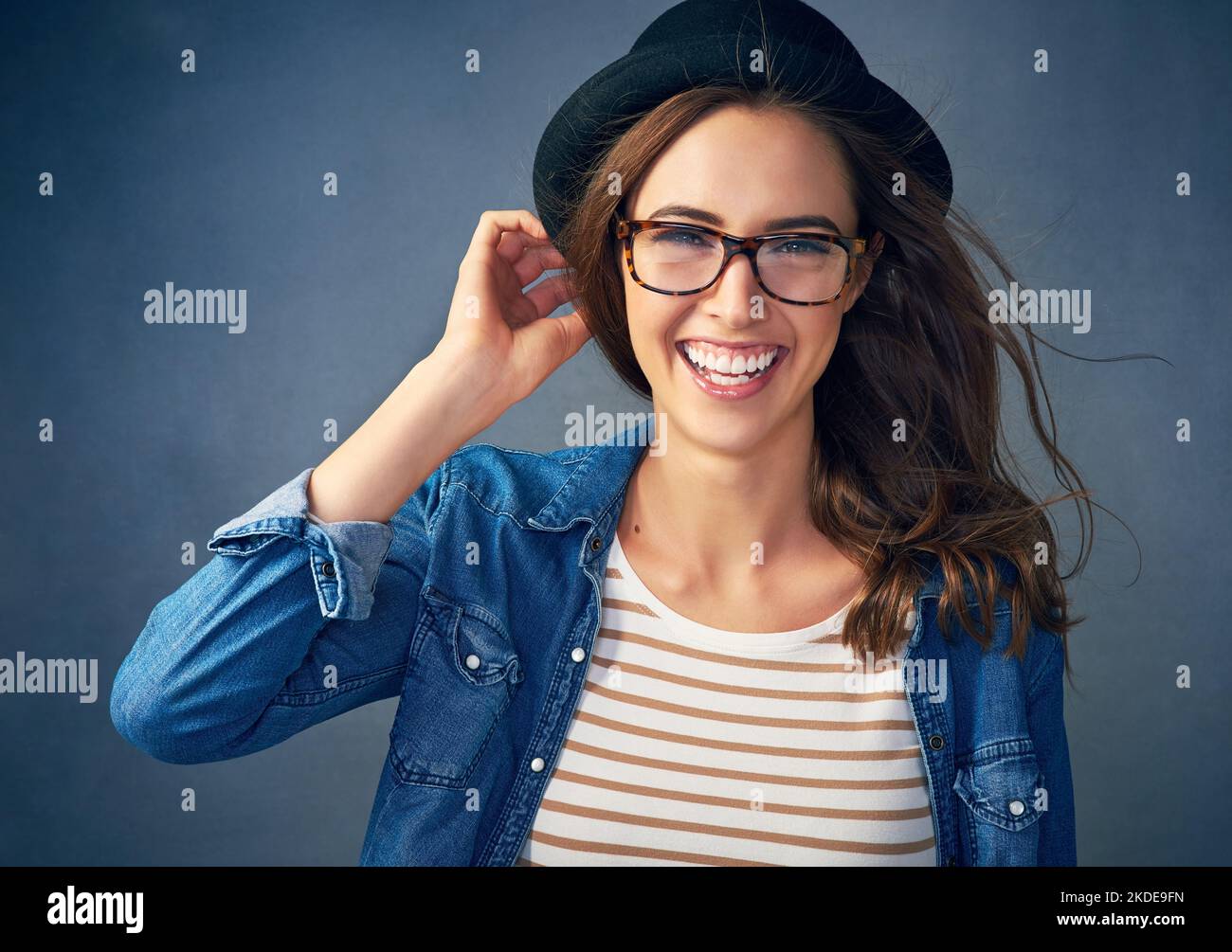 Sie sind nie ganz angezogen ohne ein Lächeln. Porträt einer schrulligen jungen Frau, die vor grauem Hintergrund im Studio lächelt. Stockfoto