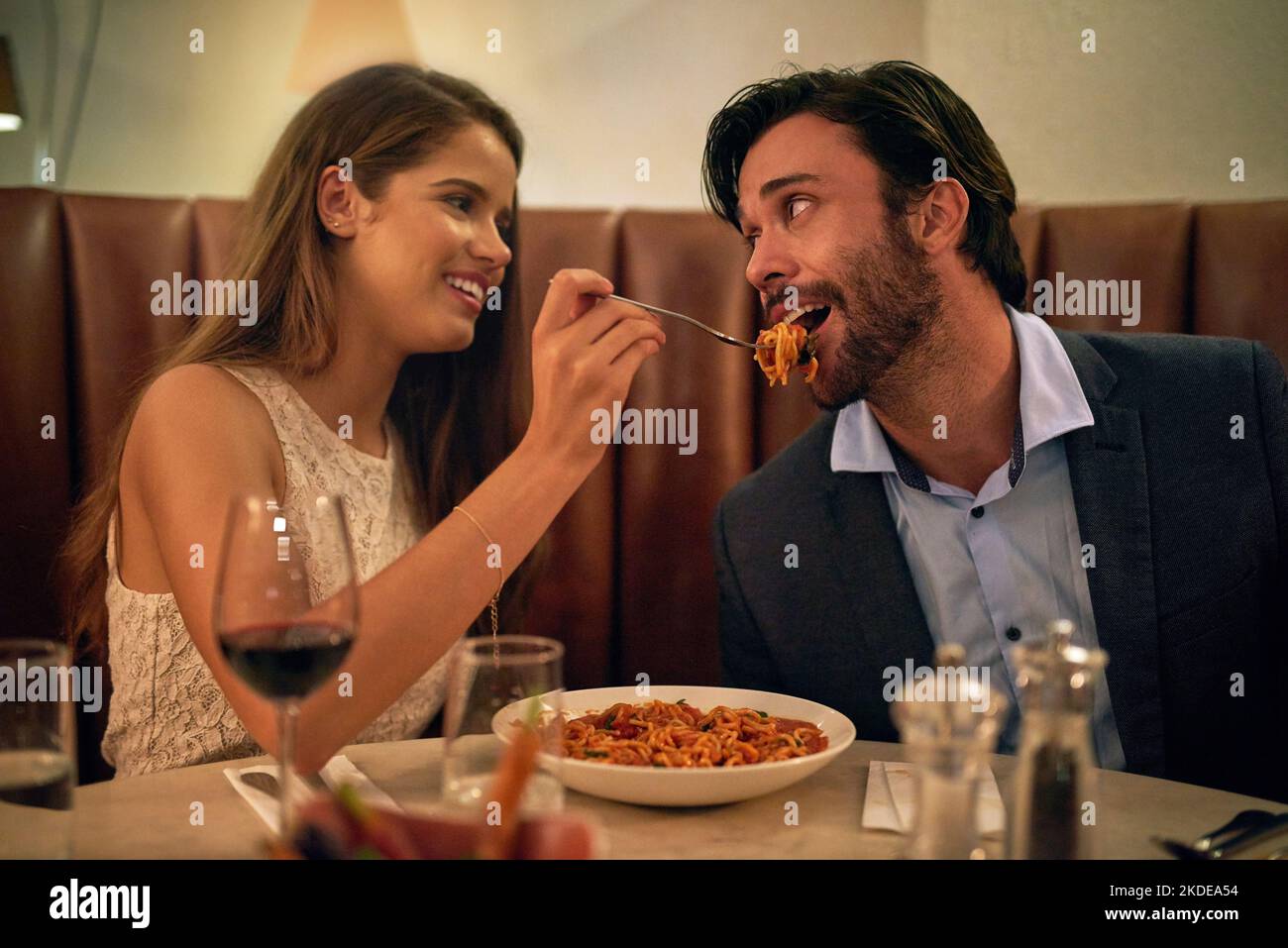 Liebe beim ersten Biss. Eine junge Frau füttert ihren Freund bei einem romantischen Dinner-Date in einem Restaurant mit einer Gabel voller Spaghetti. Stockfoto