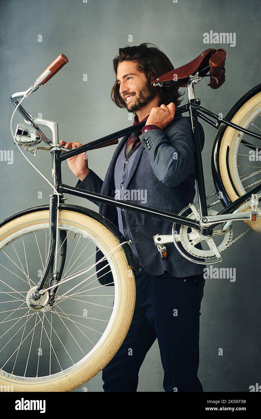 Zeit, um auf die Straße zu gehen. Studioaufnahme eines stilvoll gekleideten, hübschen jungen Mannes, der sein Fahrrad trägt. Stockfoto