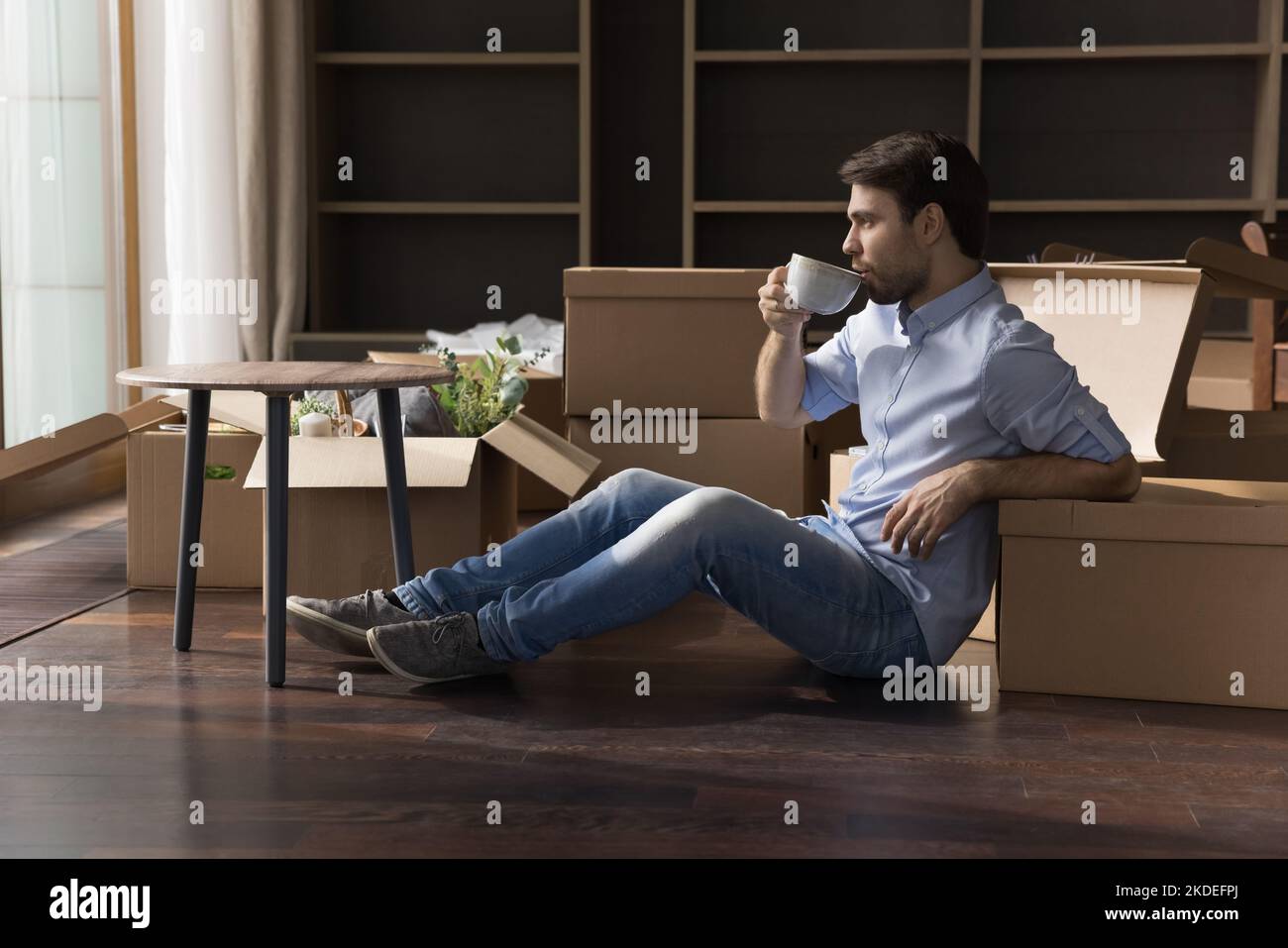 Mann, der sich mit einem Kaffeebecher in der Nähe von Pappkartons entspannt Stockfoto