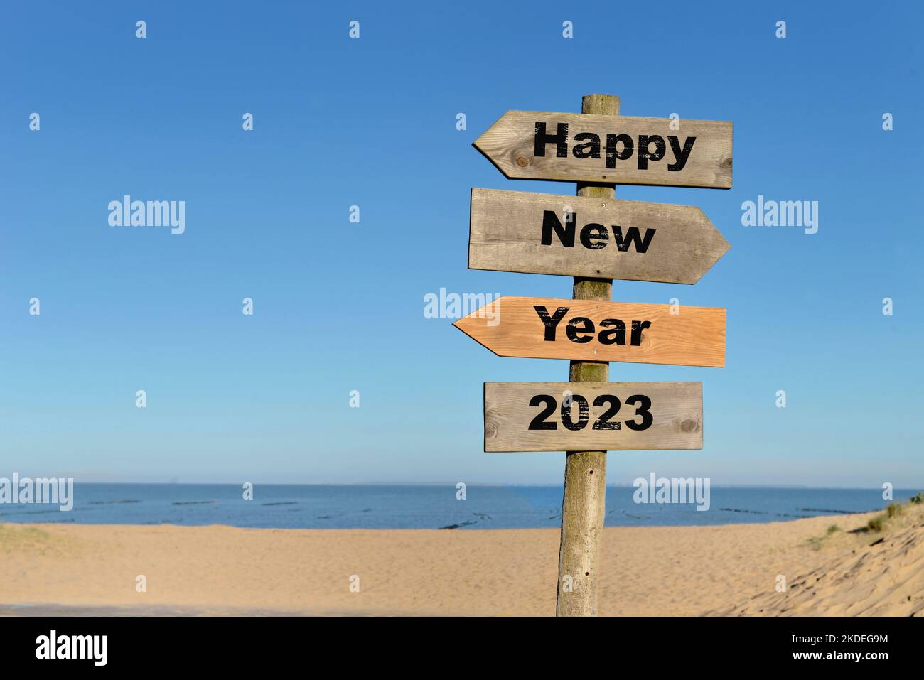 2023 ein glückliches neues Jahr steht auf einem Richtungsschild vor einem Strand am blauen Himmel Stockfoto