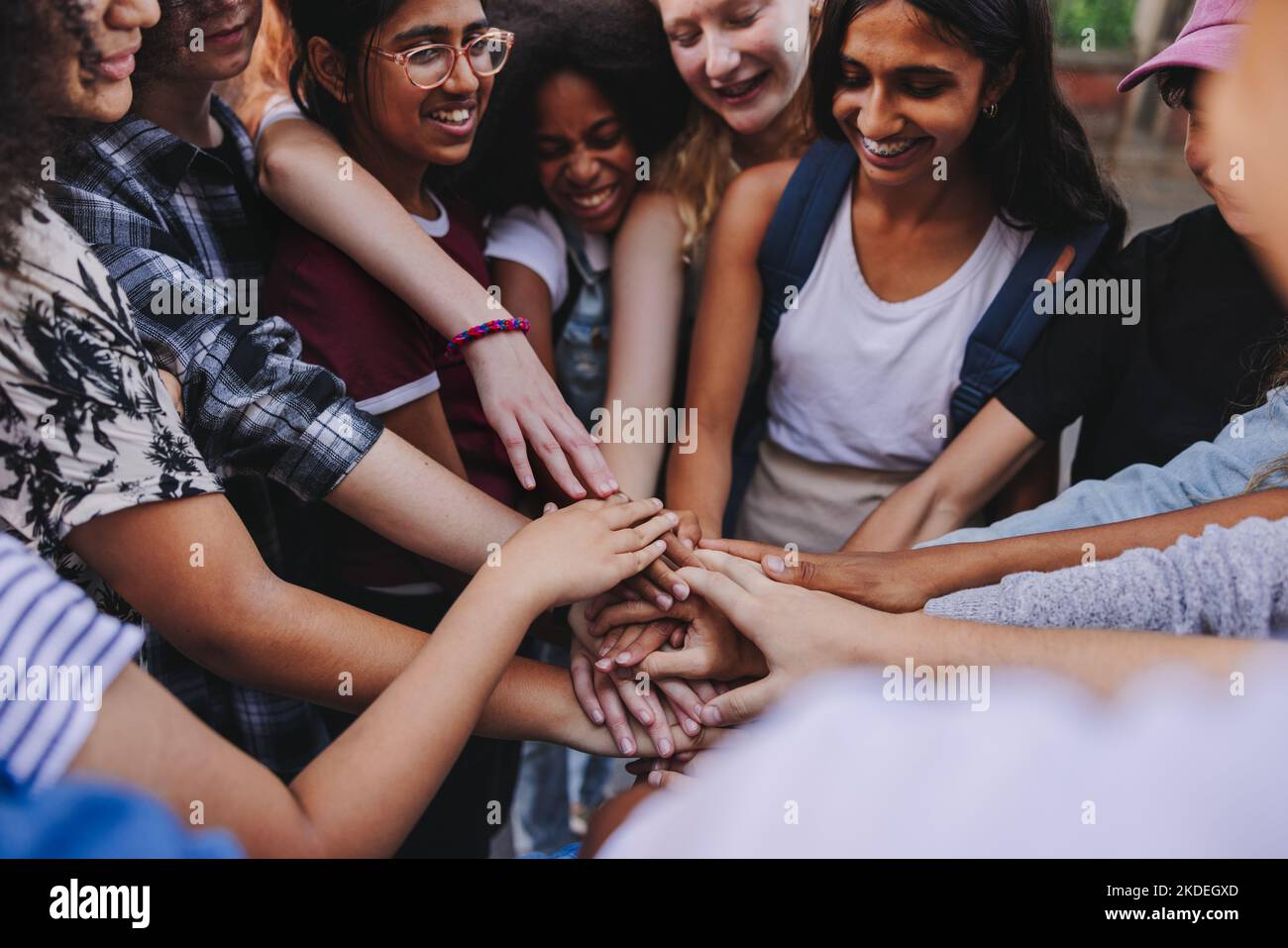 Multikulturelle Jugendliche lächeln fröhlich, während sie ihre Hände in einer Hudle zusammenlegen. Gruppe von Jugendlichen der Generation z stapeln ihre Hände auf o Stockfoto