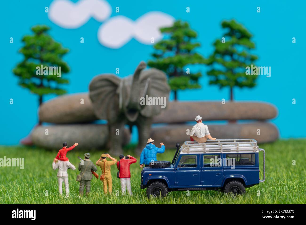 Miniatur-Spielzeug einer Gruppe von Menschen auf Safari-Reise beobachten loxodonta afrikanischen Elefanten - ein Jäger, Vater und Sohn auf der Schulter reiten, Fotograf mit Stockfoto