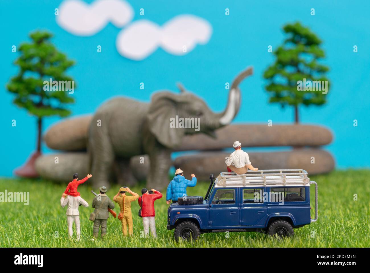 Miniatur-Spielzeug einer Gruppe von Menschen auf Safari-Reise beobachten loxodonta afrikanischen Elefanten - ein Jäger, Vater und Sohn auf der Schulter reiten, Fotograf mit Stockfoto