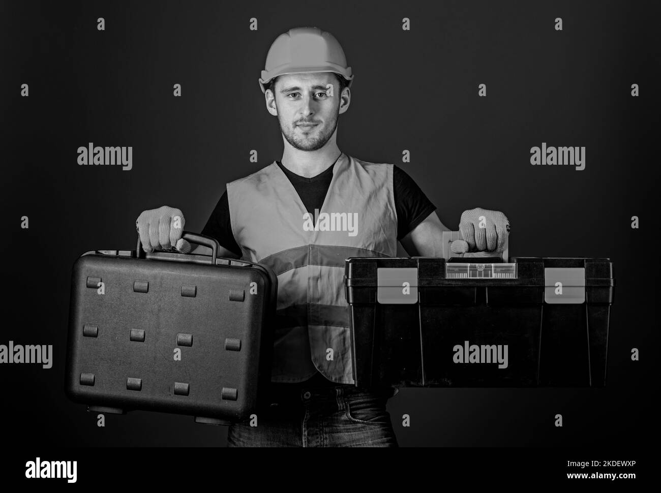Mann im Helm, Hut hält Werkzeugkasten und Koffer mit Werkzeugen, blauer Hintergrund. Toolbox und Gerätekonzept. Arbeiter, Werkstatt, Werkstatt, Baumeister Stockfoto