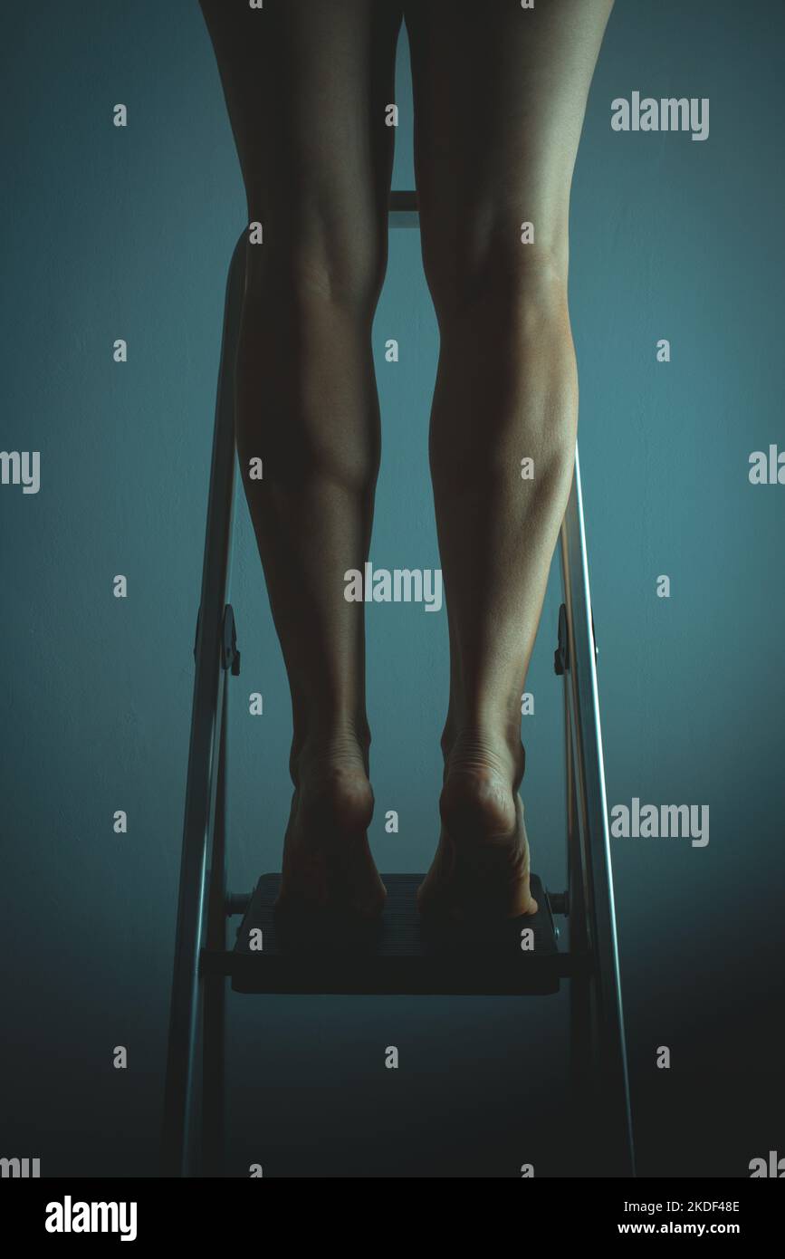 Rückansicht einer Frau, die barfuß auf Zehenspitzen auf einer Leiter steht Stockfoto