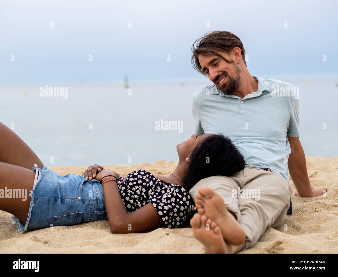 Heterosexuell vielfältiges junges Paar, das liebevoll vor dem Meer sitzt Stockfoto