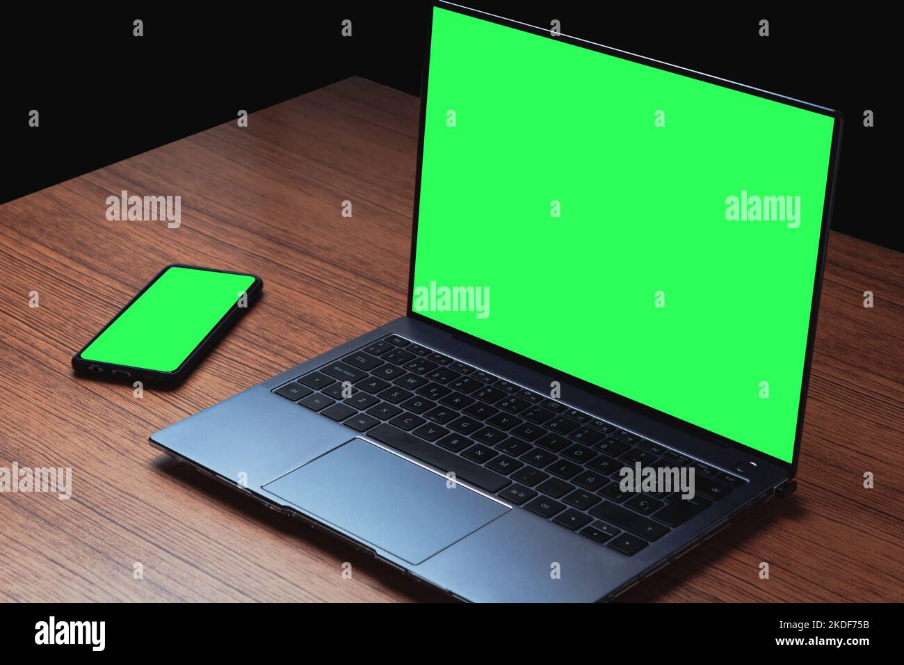 Mockup Bild mit grünem Bildschirm auf Computer und Smartphone auf Holz Schreibtisch. Hintergrund für Werbetext. Platz für Design. Stockfoto