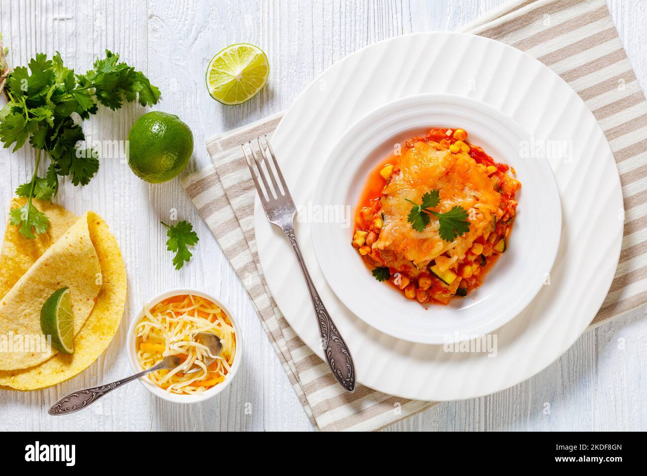 Vegetarische Enchilada-Kasserolle mit Tortillas, Sauce, Pinto-Bohnen, Mais, Zucchini und mexikanischem Käse auf weißem Teller, flacher Laie Stockfoto