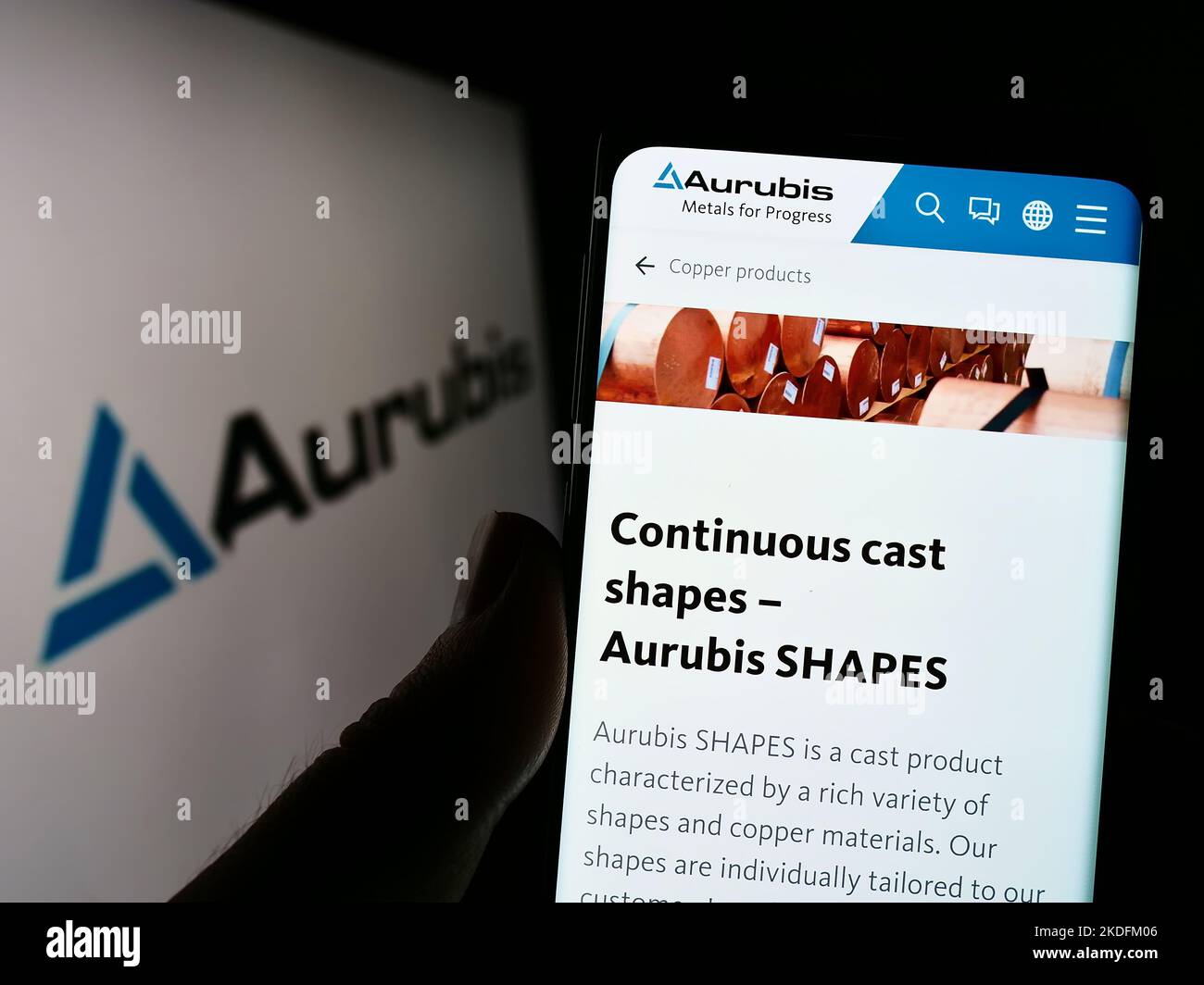 Person, die Mobiltelefon mit Website des deutschen Kupferunternehmens Aurubis AG auf dem Bildschirm vor dem Unternehmenslogo hält. Konzentrieren Sie sich auf die Mitte des Telefondisplays. Stockfoto