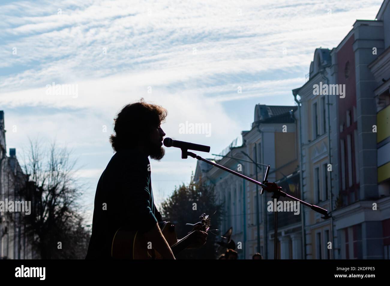 Silhouette eines Straßenmusikers, der im Mikrofon auf unscharfem Hintergrund von Stadtstraßengebäuden und blauem Himmel singt. Ukraine, Zhytomyr, 04. November 2022 Stockfoto