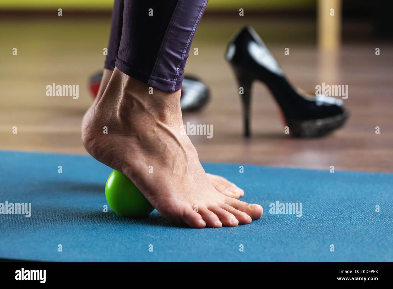 Eine Frau führt eine Fußmuskelmassage mit einem Massageball durch, während sie im Studio auf einer Matte steht. Prävention von müde Beine, geschwollene Venen nach Ermüdung Stockfoto