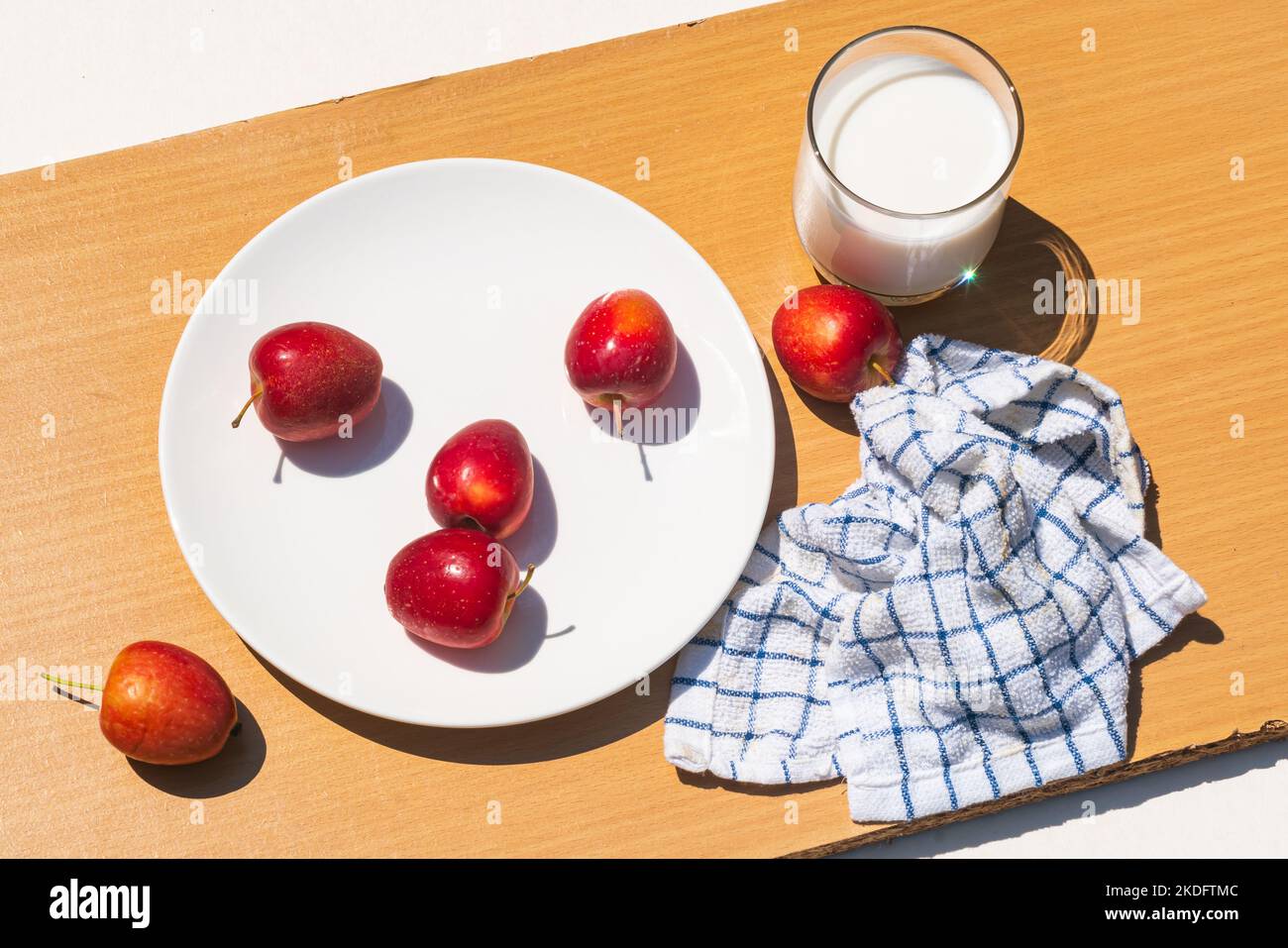 Frischer, reifer Mini-Apfel oder Krabapfel mit frischer Milch in einem transparenten Glas auf Holzschneidebrett in direkter Sonneneinstrahlung. Stockfoto