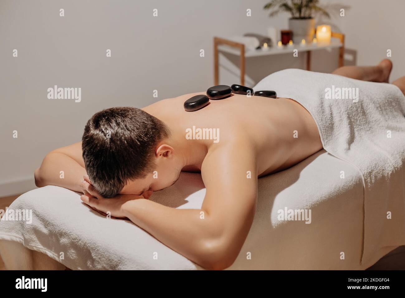 Schöner Mann, der sich während einer Rückenmassage mit heißen Steinen entspannt. Körperpflege und SPA im Resort. Stockfoto