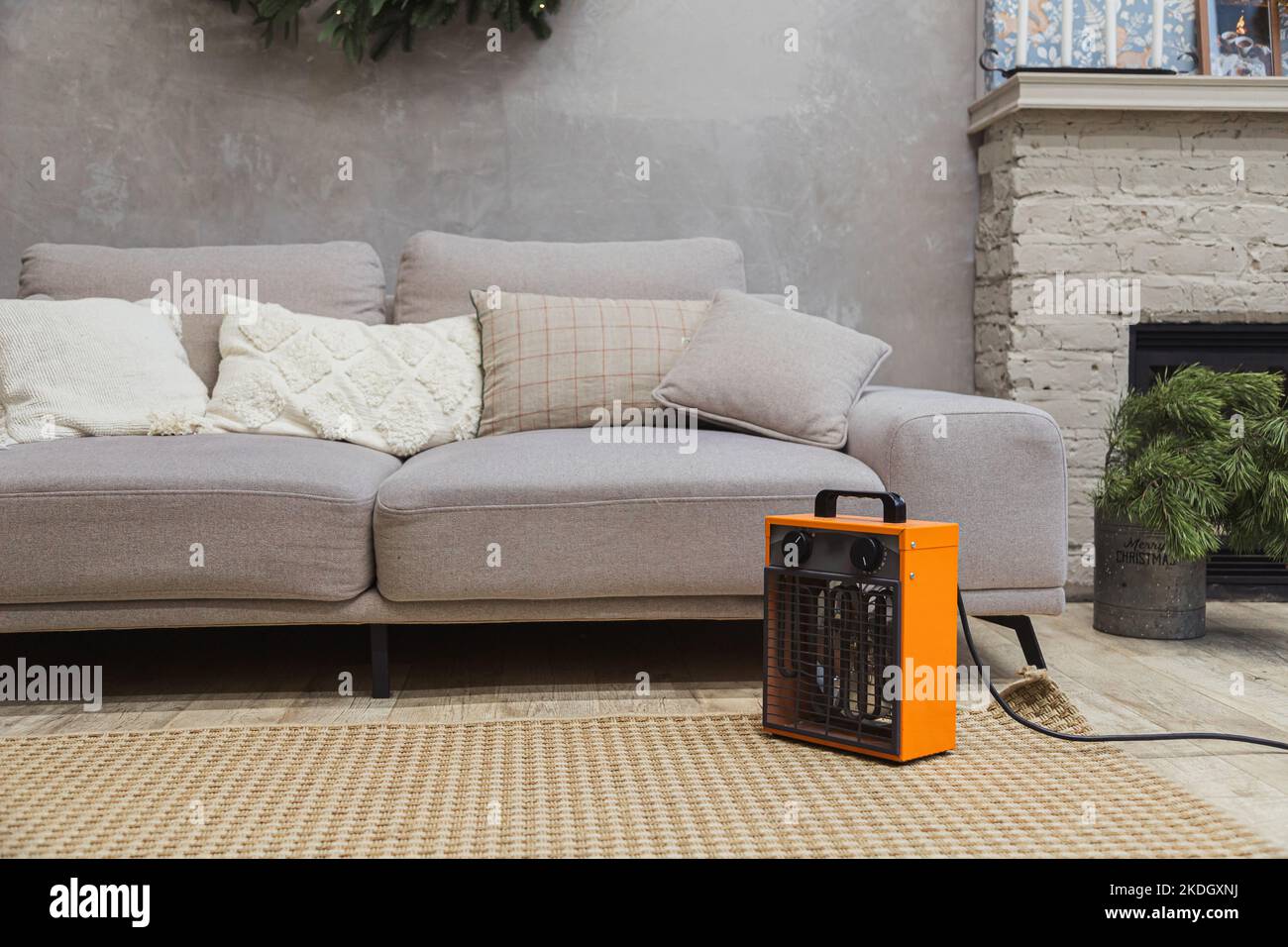 Elektrischer Heizlüfter auf dem Boden im Wohnzimmer mit Couch und Kamin Stockfoto