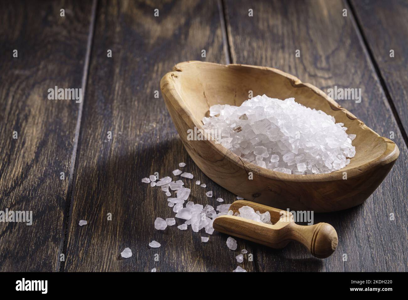 Grobes Salz mit einem Messlöffel in einer Holzschüssel auf einem Eichentisch Stockfoto