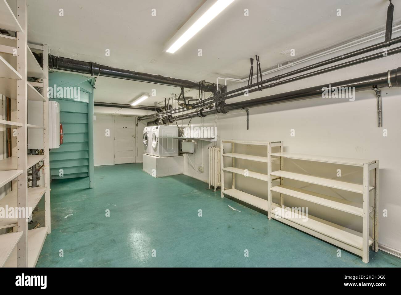 Kesselraum eines Mehrfamilienhauses mit Rohren und Messgeräten. Ein langer Raum mit technischer Kommunikation und mit Waschmaschine in der modernen Wohnung Stockfoto