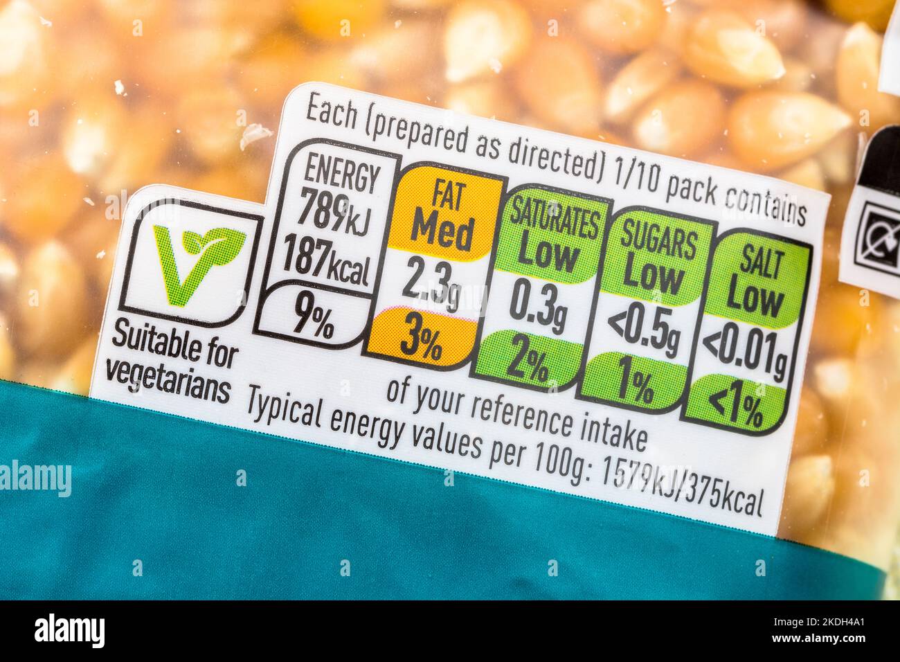 Plastikpaket von ASDA Supermarkt eigenen Etikett gelben Popcornkörnern mit Lebensmitteln Ampel. Logo für vegane Lebensmittel, Ampeletikett. Stockfoto