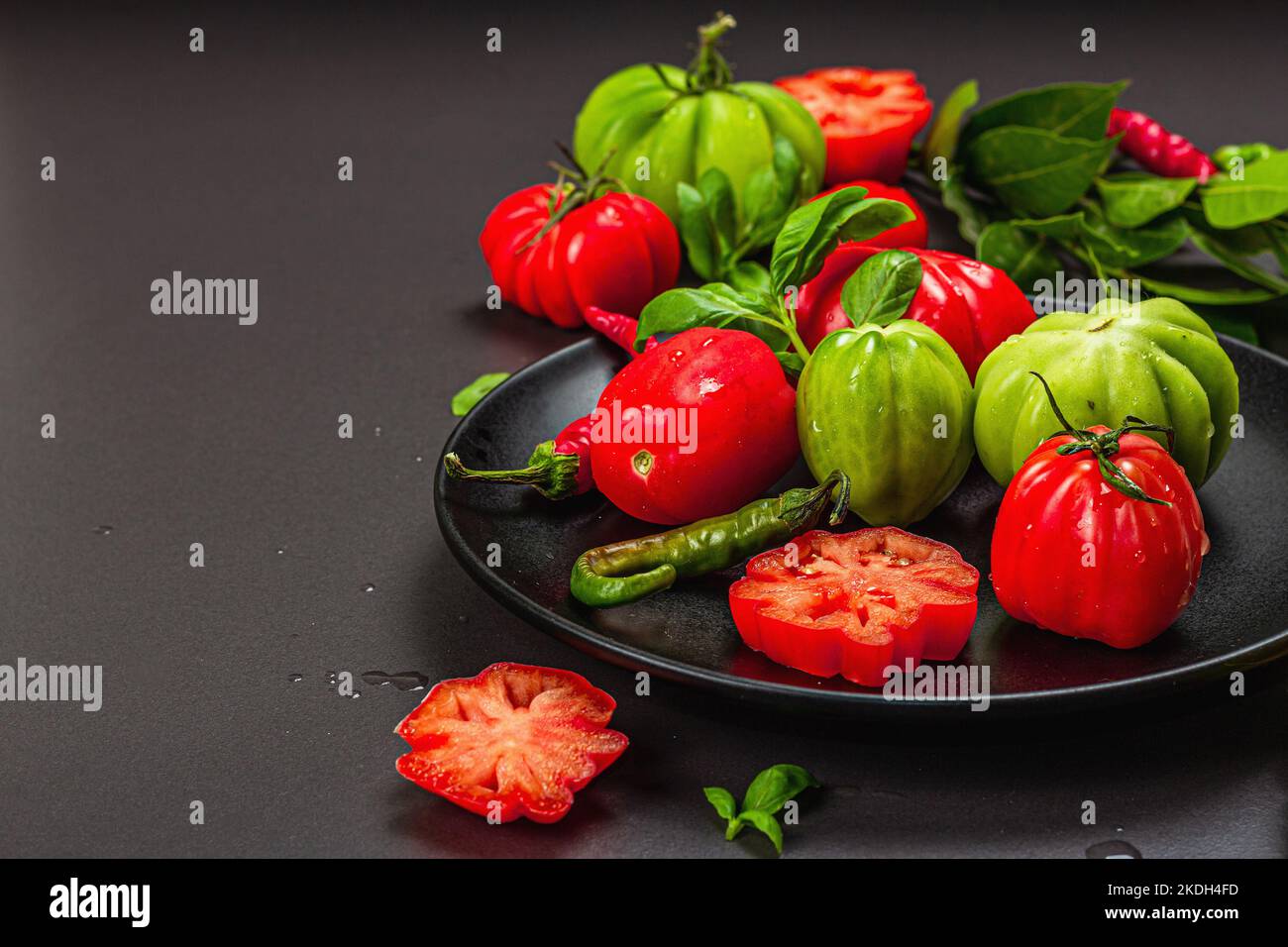 Grüne und rote gerippte Tomaten, amerikanische oder florentinische Sorte. Reifes Gemüse, Chili, frische Lorbeerblätter. Trendiges hartes Licht, dunkler Schatten, Steinbeton Stockfoto