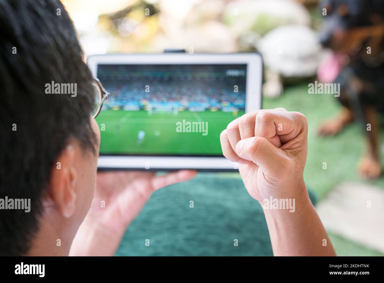 Mann mit der Faust auf, aufgeregt beim Betrachten von Fußballsportspielen auf dem digitalen Tablet. Online- oder digitales Lifestyle-Konzept. Stockfoto