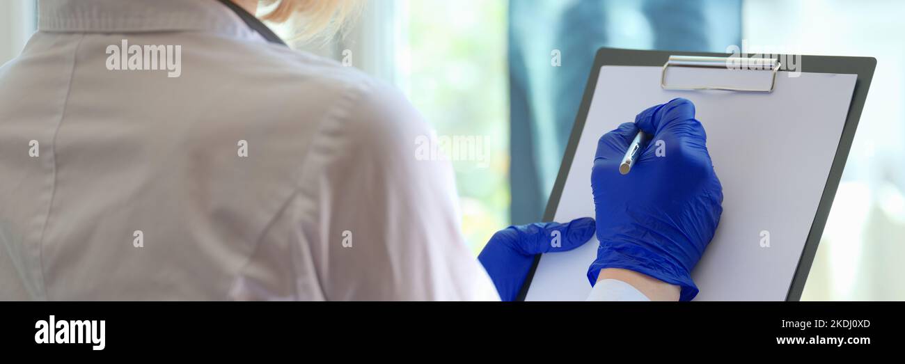 Die Hand des Arztes schreibt Notizen auf das Clipboard in der Medizin und schaut durch den Röntgenfilm Stockfoto