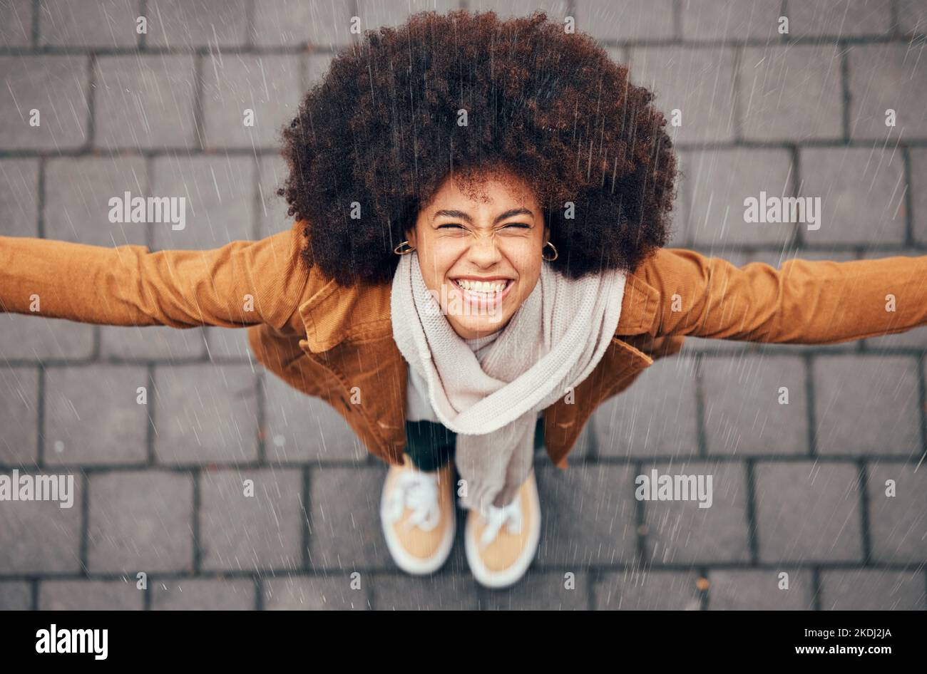 Schwarze Frau, stehen zu regen und glücklich in der Stadt im Winter mit Lächeln, Afro oder trendige Mode fühlen. Frau, draußen oben oder Glück im Nieselregen, Splash Stockfoto