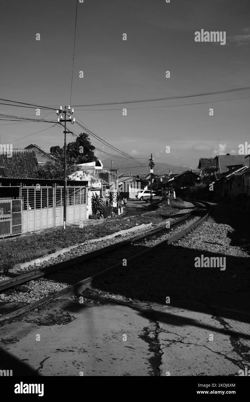 Schwarzweißfoto, Schwarzweißfoto einer Zugstrecke, die durch Wohngebiete in der Gegend von Cikancung führt - Indonesien Stockfoto