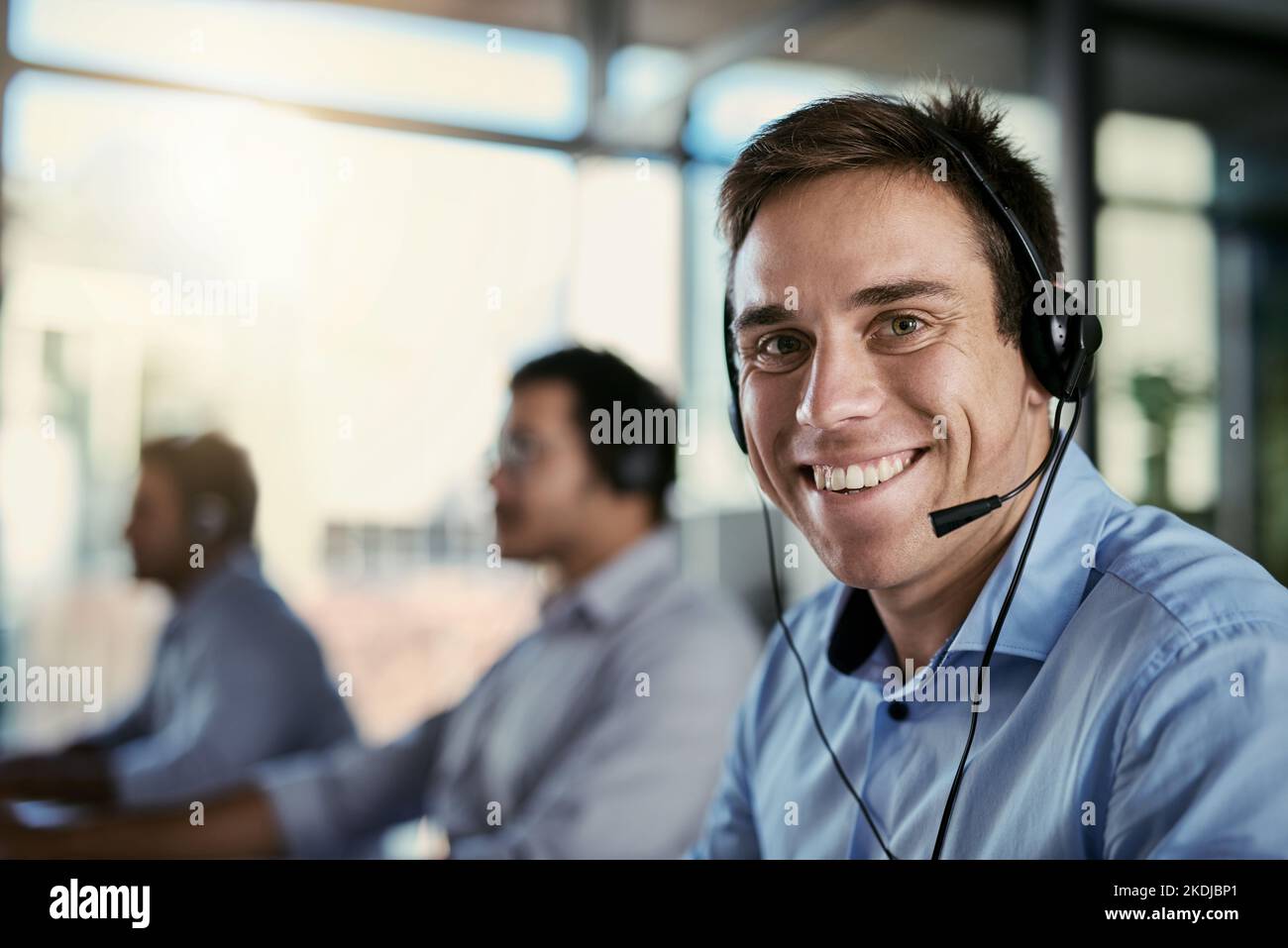 Standen zur Verfügung, um Ihren Anruf anzunehmen. Porträt eines Call Center-Agenten, der in einem Büro arbeitet, mit seinen Kollegen im Hintergrund. Stockfoto